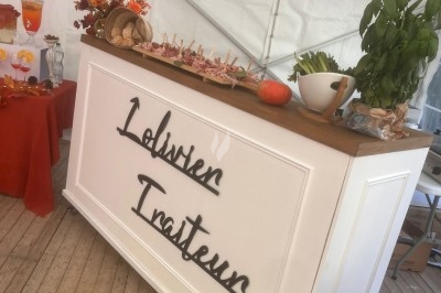 Des invités assis à des tables décorées de fleurs et feuillages d'automne dans une grande tente lumineuse.