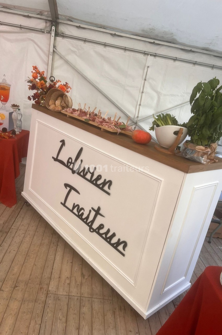 Comptoir de traiteur décoré avec des aliments, des plantes aromatiques et des éléments automnaux sous une tente.