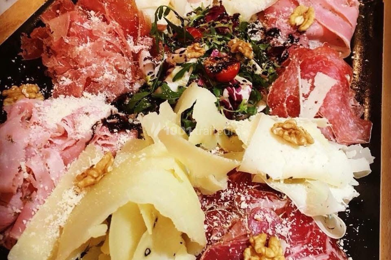 Plateau de charcuterie et fromages variés garnis de noix, herbes fraîches et copeaux de parmesan.