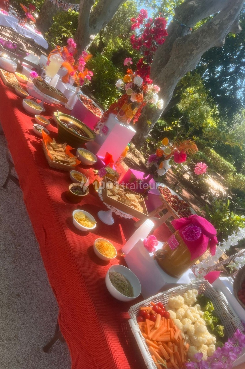 Table garnie de plats variés, sauces et légumes, installée en extérieur avec une décoration florale colorée.