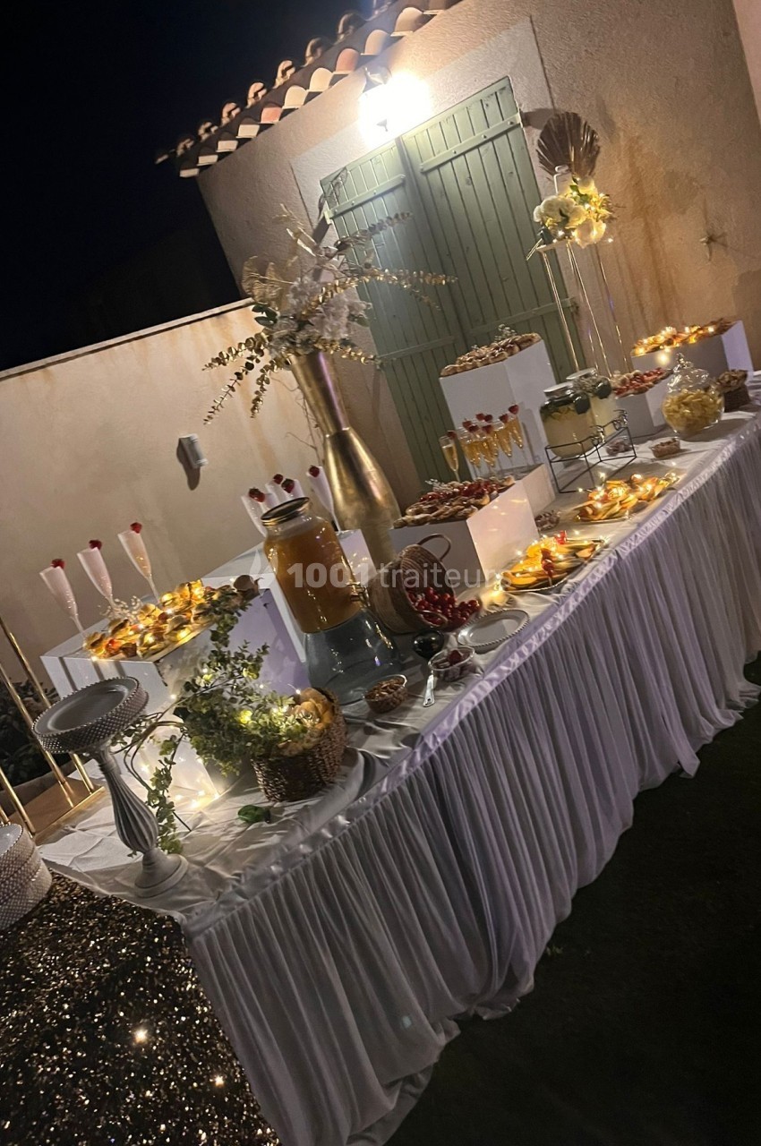 Table décorée pour une réception en extérieur, avec desserts, boissons et éclairage chaleureux en soirée.