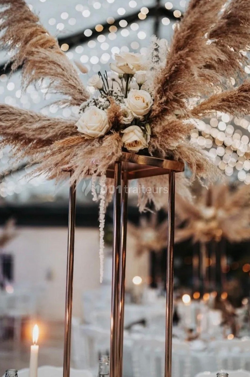 Centre de table avec des pampas, des roses blanches et des lumières suspendues dans une ambiance de soirée festive.