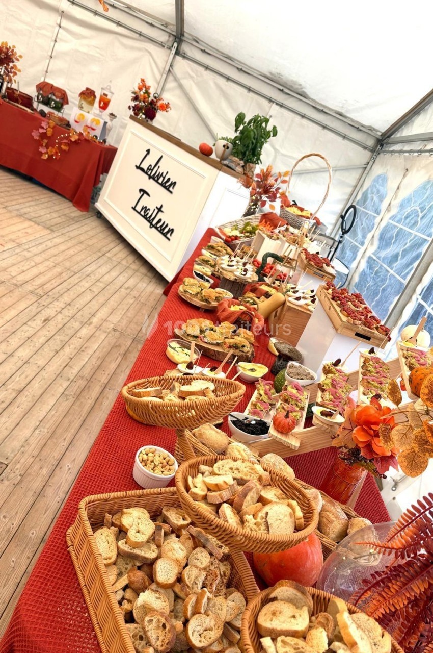 Buffet automnal sous une tente, avec pains, fruits, desserts et décorations aux tons chauds.