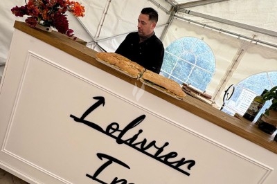 Des invités assis à des tables décorées de fleurs et feuillages d'automne dans une grande tente lumineuse.