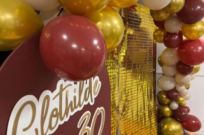 Tables de pique-nique en bois sur une terrasse en béton, entourées de pelouse et d'arbres sous un ciel nuageux.