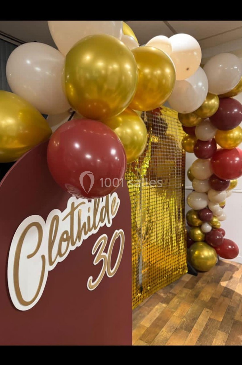 Décoration d'anniversaire avec arche de ballons dorés, rouges et blancs, et panneau personnalisé ’Clothilde 30’.