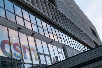Bâtiment moderne avec façades vitrées, espaces verts et escaliers extérieurs dans un environnement urbain.