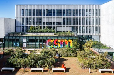 Bâtiment moderne avec façades vitrées, espaces verts et escaliers extérieurs dans un environnement urbain.