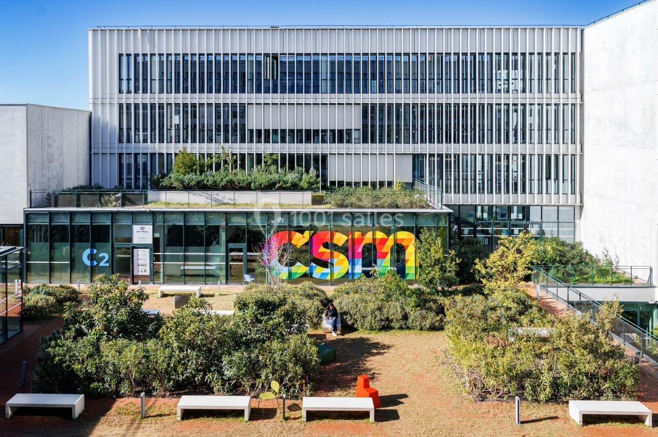 Façade moderne d'un bâtiment avec une végétation sur le toit et un logo coloré ’CSM’ sur une baie vitrée.