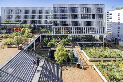 Bâtiment moderne avec façades vitrées, espaces verts et escaliers extérieurs dans un environnement urbain.