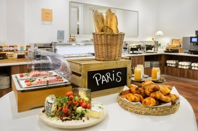 Buffet de petit-déjeuner avec viennoiseries, fromages, charcuterie, pain et confitures, dans une salle lumineuse.