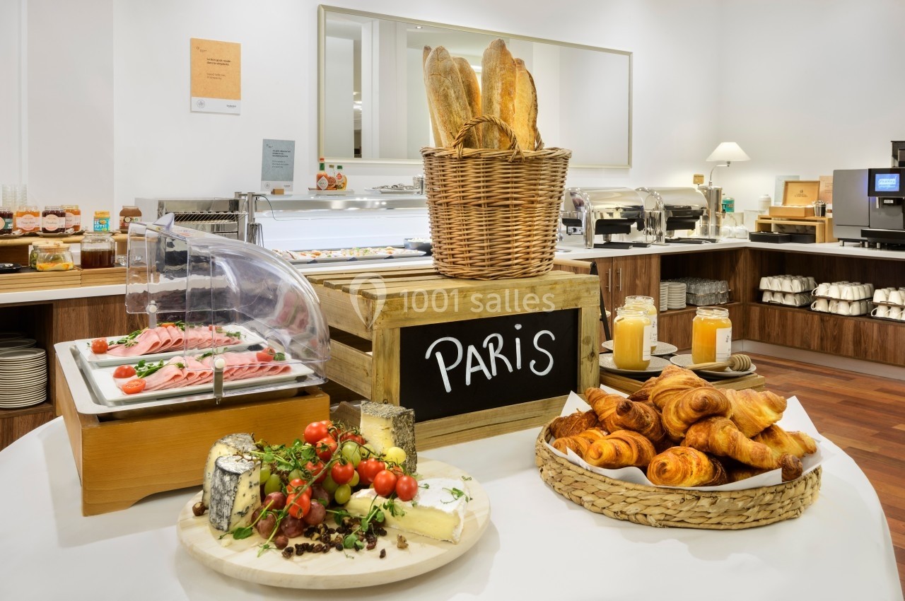 Buffet de petit-déjeuner avec viennoiseries, fromages, charcuterie, pain et confitures, dans une salle lumineuse.