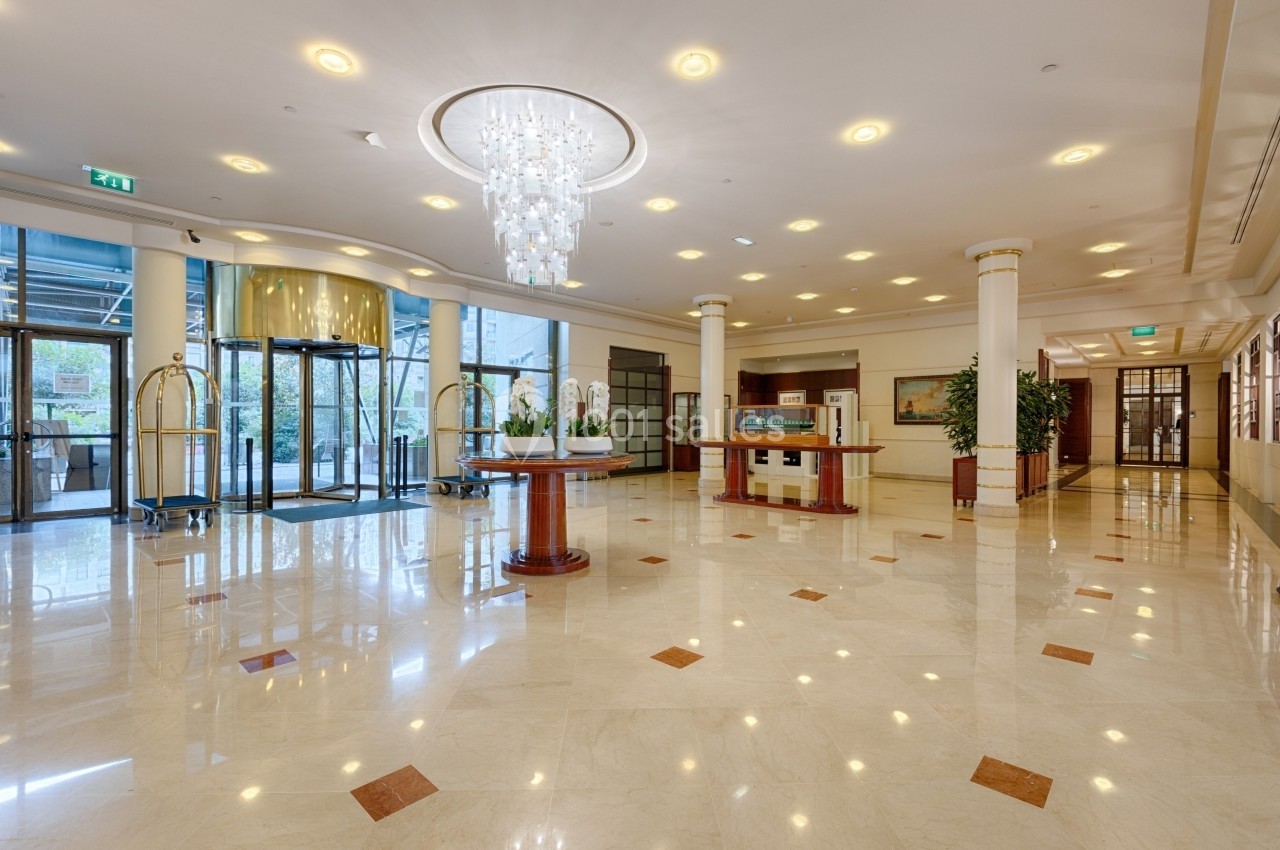 Hall d'entrée spacieux avec sol en marbre, lustre central, comptoir d'accueil et portes vitrées donnant sur l'extérieur.