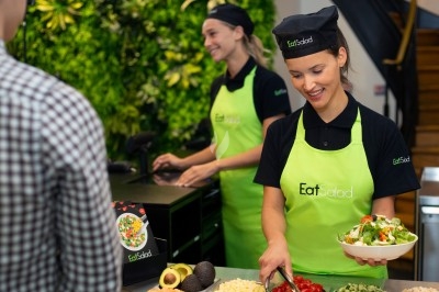 Deux employées en tablier vert préparent des salades fraîches dans un restaurant devant un client.