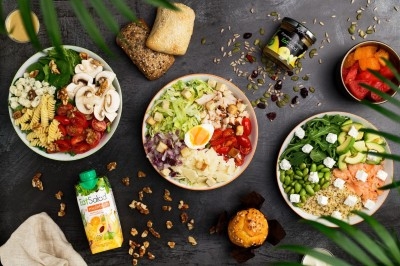 Assortiment de salades variées avec légumes, œuf, fromage, pain et boissons sur une table sombre décorée de feuilles.