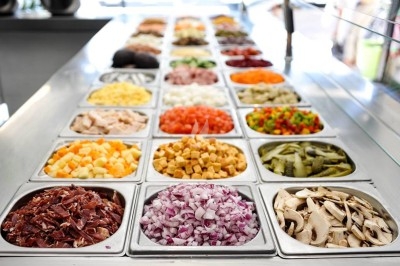 Bacs remplis d'ingrédients variés comme légumes, fromages et viandes, disposés sur un comptoir de préparation.