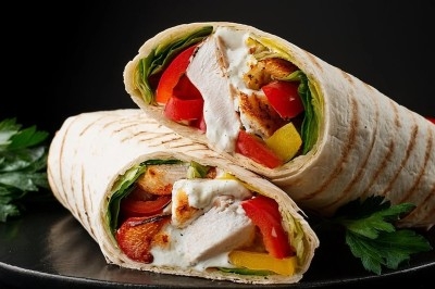 Deux wraps garnis de poulet grillé, légumes colorés et sauce blanche, présentés sur un fond sombre avec des herbes.