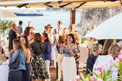 Terrasse en bord de mer avec tables dressées, chaises en osier et parasols sous un ciel ensoleillé.