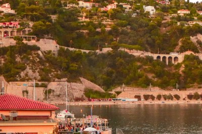 Terrasse en bord de mer avec tables dressées, chaises en osier et parasols sous un ciel ensoleillé.