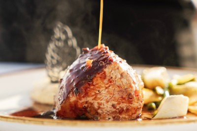 Terrasse en bord de mer avec tables dressées, chaises en osier et parasols sous un ciel ensoleillé.