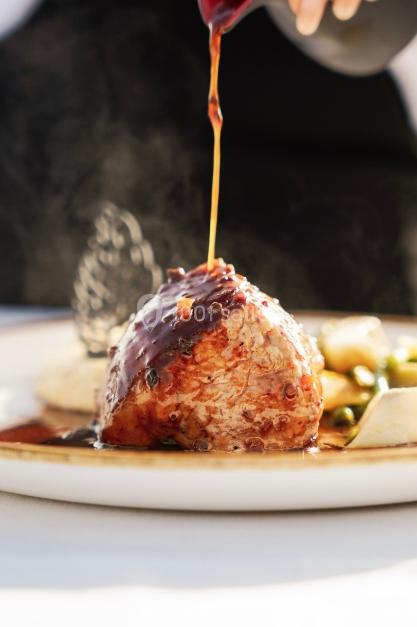 Viande nappée de sauce servie avec des légumes et une purée, présentée dans une assiette blanche.