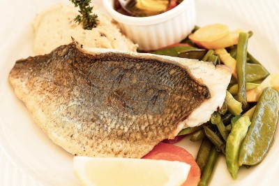 Terrasse en bord de mer avec tables dressées, chaises en osier et parasols sous un ciel ensoleillé.