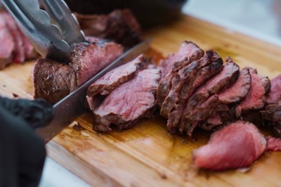 Terrasse en bord de mer avec tables dressées, chaises en osier et parasols sous un ciel ensoleillé.