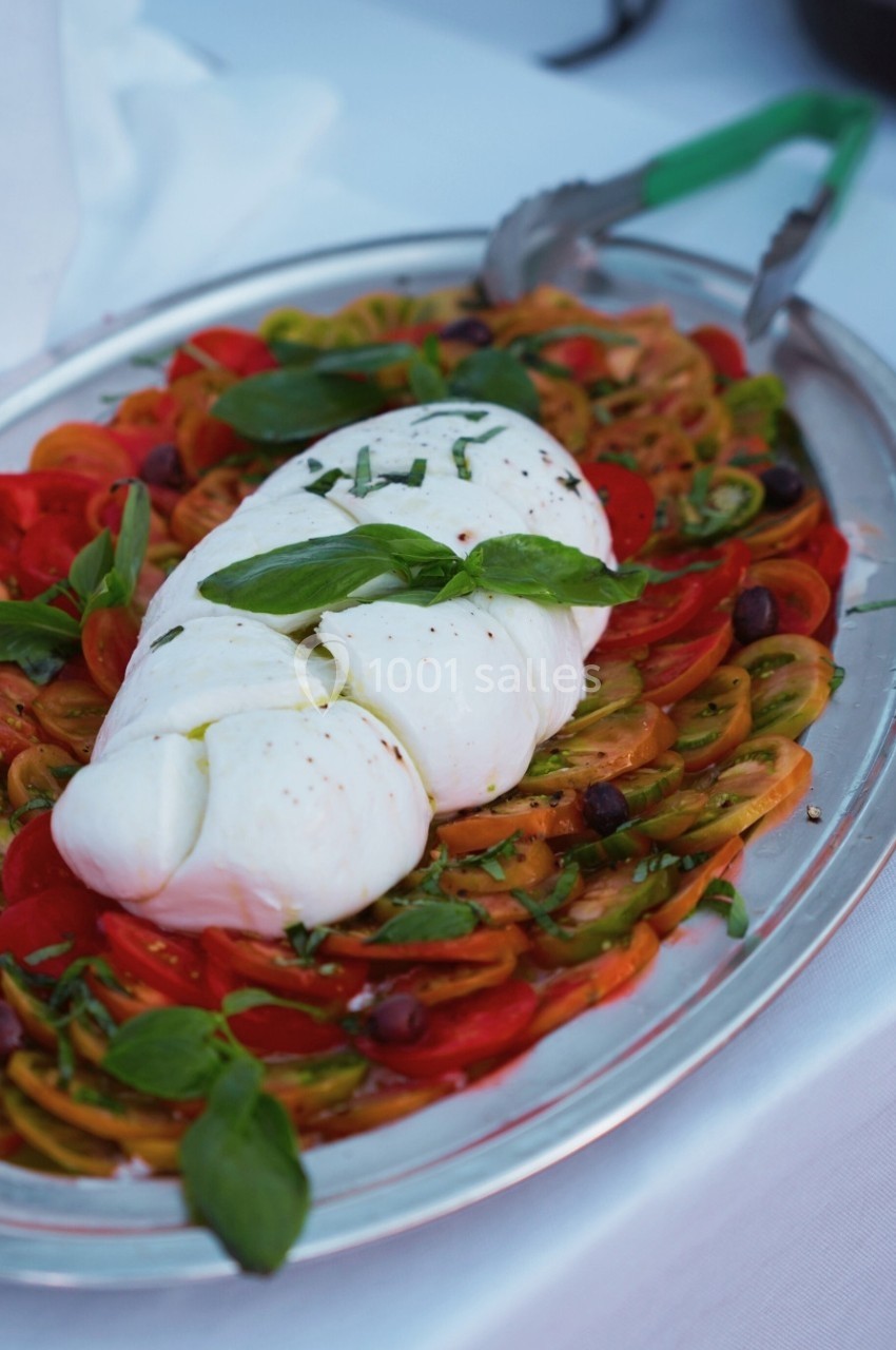 Assiette de tomates colorées garnie de burrata, basilic frais et olives, présentée sur un plat en métal.