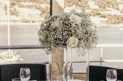 Terrasse en bord de mer avec tables dressées, chaises en osier et parasols sous un ciel ensoleillé.
