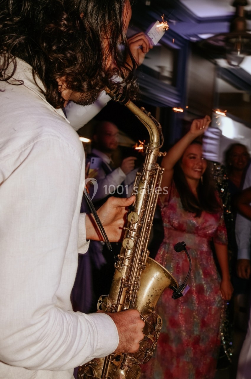 Un musicien joue du saxophone lors d'une fête, entouré de personnes tenant des cierges magiques.