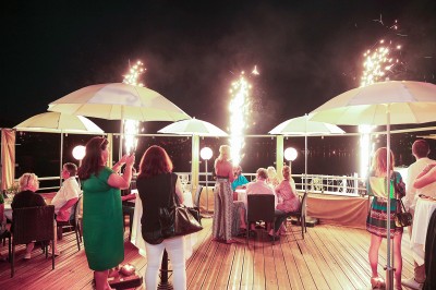 Un verre à cocktail garni d'un demi-fruit de la passion, posé sur une table dressée en extérieur.