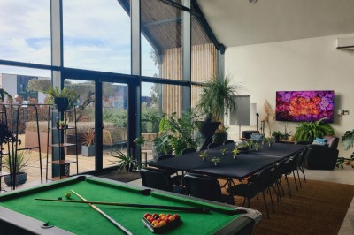 Façade d'une maison moderne en bois et verre, éclairée de nuit, avec jardin et portail en premier plan.