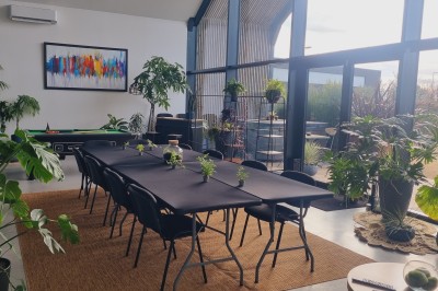 Façade d'une maison moderne en bois et verre, éclairée de nuit, avec jardin et portail en premier plan.