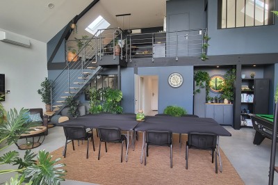 Façade d'une maison moderne en bois et verre, éclairée de nuit, avec jardin et portail en premier plan.