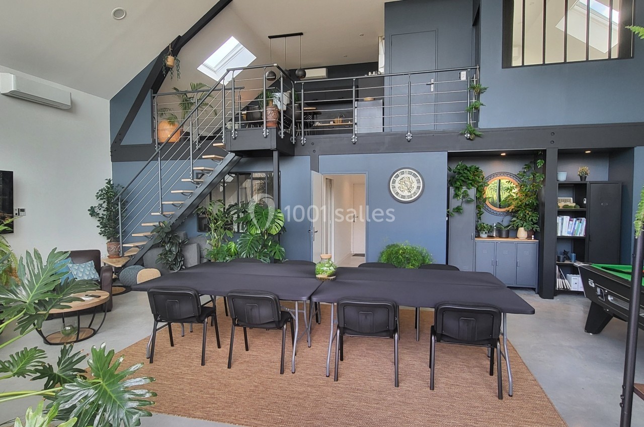 Salle à manger moderne avec une grande table, des plantes décoratives, un escalier et une mezzanine.