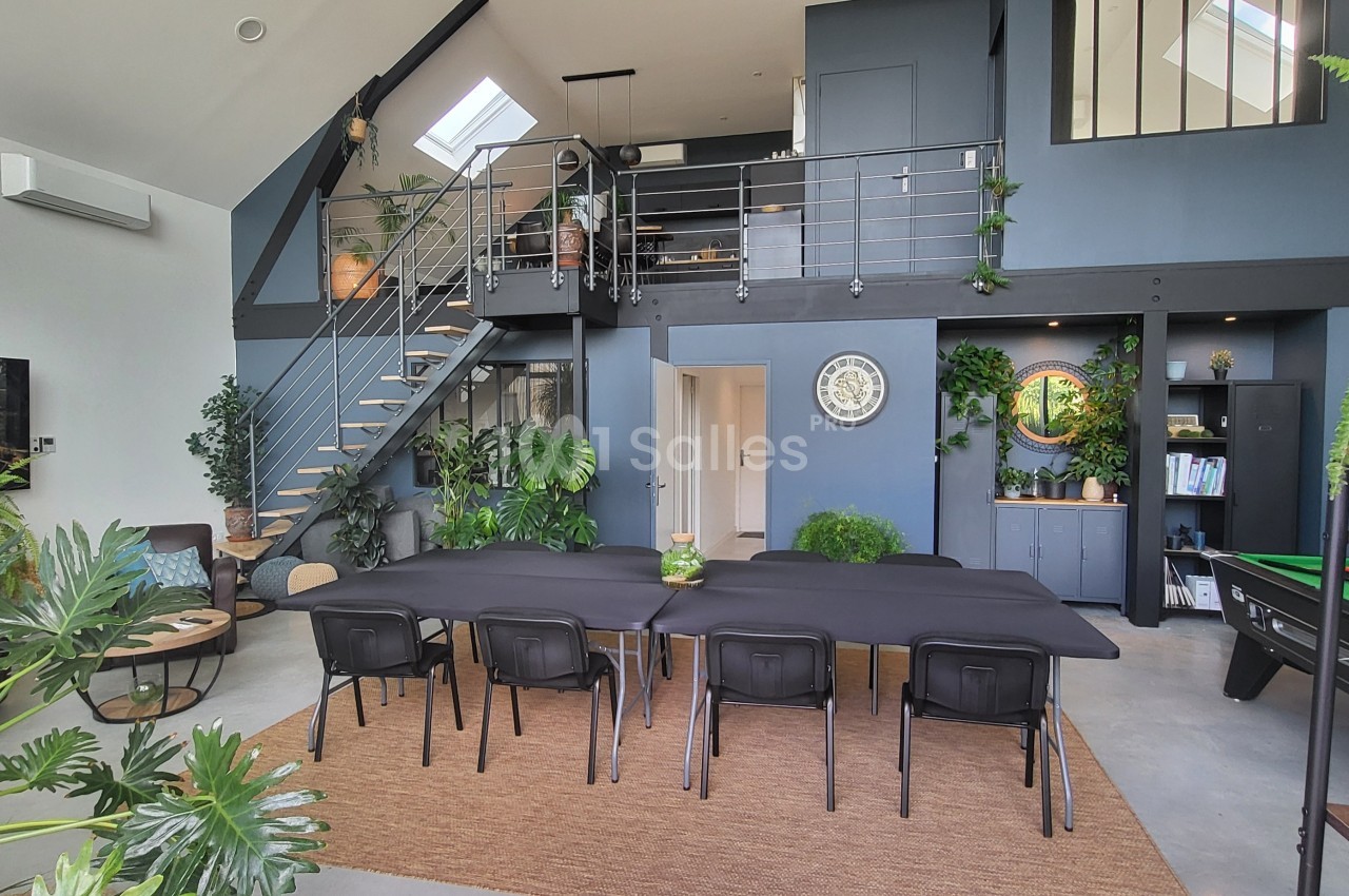 Salle à manger moderne avec une grande table, des plantes décoratives, un escalier et une mezzanine.