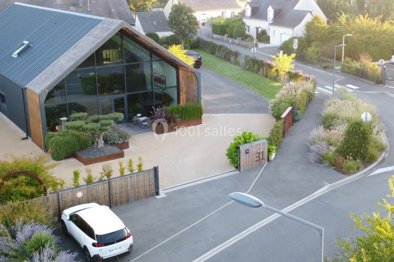 Vue aérienne d'une maison moderne avec façade vitrée, jardin paysager et voiture blanche stationnée devant.