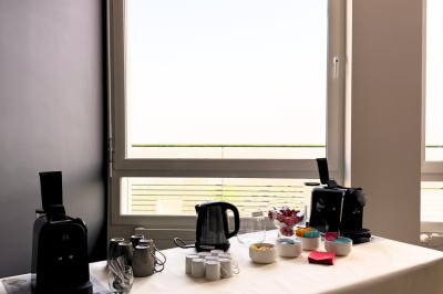 Table dressée avec cafetières, théière, tasses et condiments, placée près d'une fenêtre lumineuse.