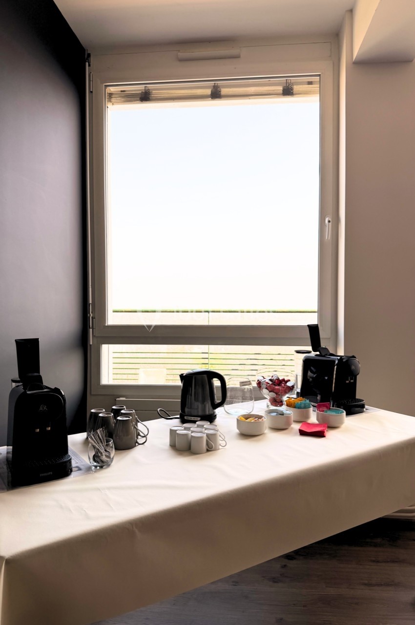 Table dressée avec cafetières, théière, tasses et condiments, placée près d'une fenêtre lumineuse.