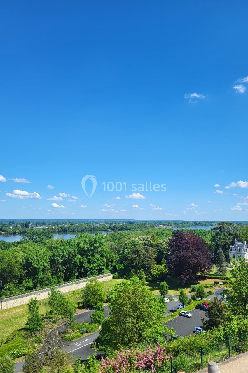 Vue panoramique sur un parc verdoyant avec des arbres, une route, un bâtiment et un ciel bleu dégagé.