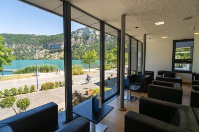 Chambre d'hôtel avec lit double, bureau, lampe, télévision murale et fenêtre donnant sur un paysage verdoyant.
