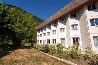 Chambre d'hôtel avec lit double, bureau, lampe, télévision murale et fenêtre donnant sur un paysage verdoyant.