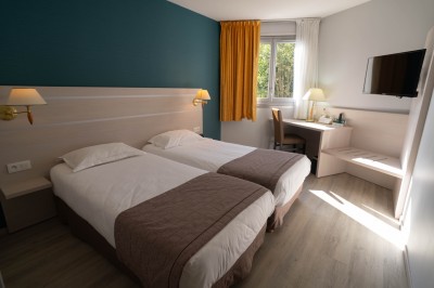 Chambre d'hôtel avec lit double, bureau, lampe, télévision murale et fenêtre donnant sur un paysage verdoyant.