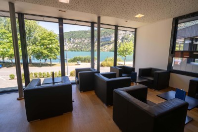 Chambre lumineuse avec lit double, bureau, chaise, télévision murale et fenêtre donnant sur un espace vert.