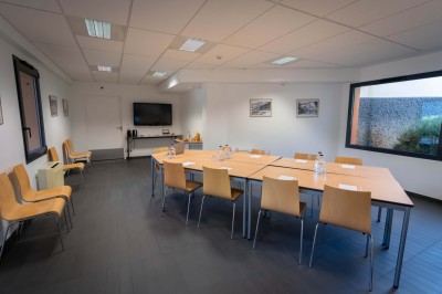 Chambre lumineuse avec lit double, bureau, chaise, télévision murale et fenêtre donnant sur un espace vert.