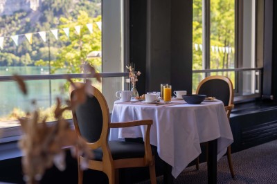 Chambre lumineuse avec lit double, bureau, chaise, télévision murale et fenêtre donnant sur un espace vert.