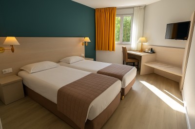 Chambre lumineuse avec lit double, bureau, chaise, télévision murale et fenêtre donnant sur un espace vert.