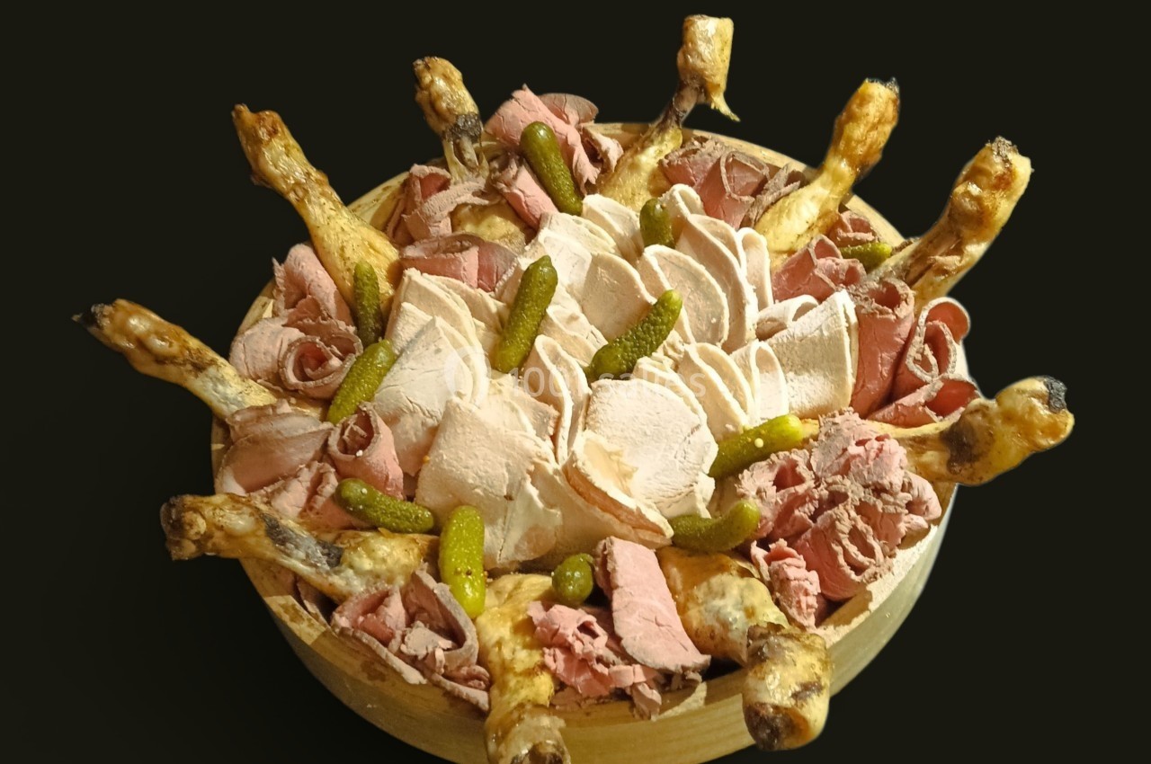 Plateau de charcuterie avec cuisses de volaille, tranches de viande froide et cornichons, présenté sur un fond noir.