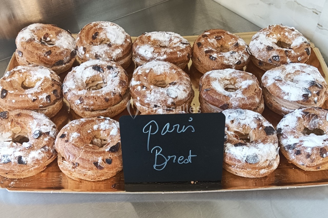 Plateau de Paris-Brest garnis, saupoudrés de sucre glace, exposés sur un comptoir avec une étiquette manuscrite.