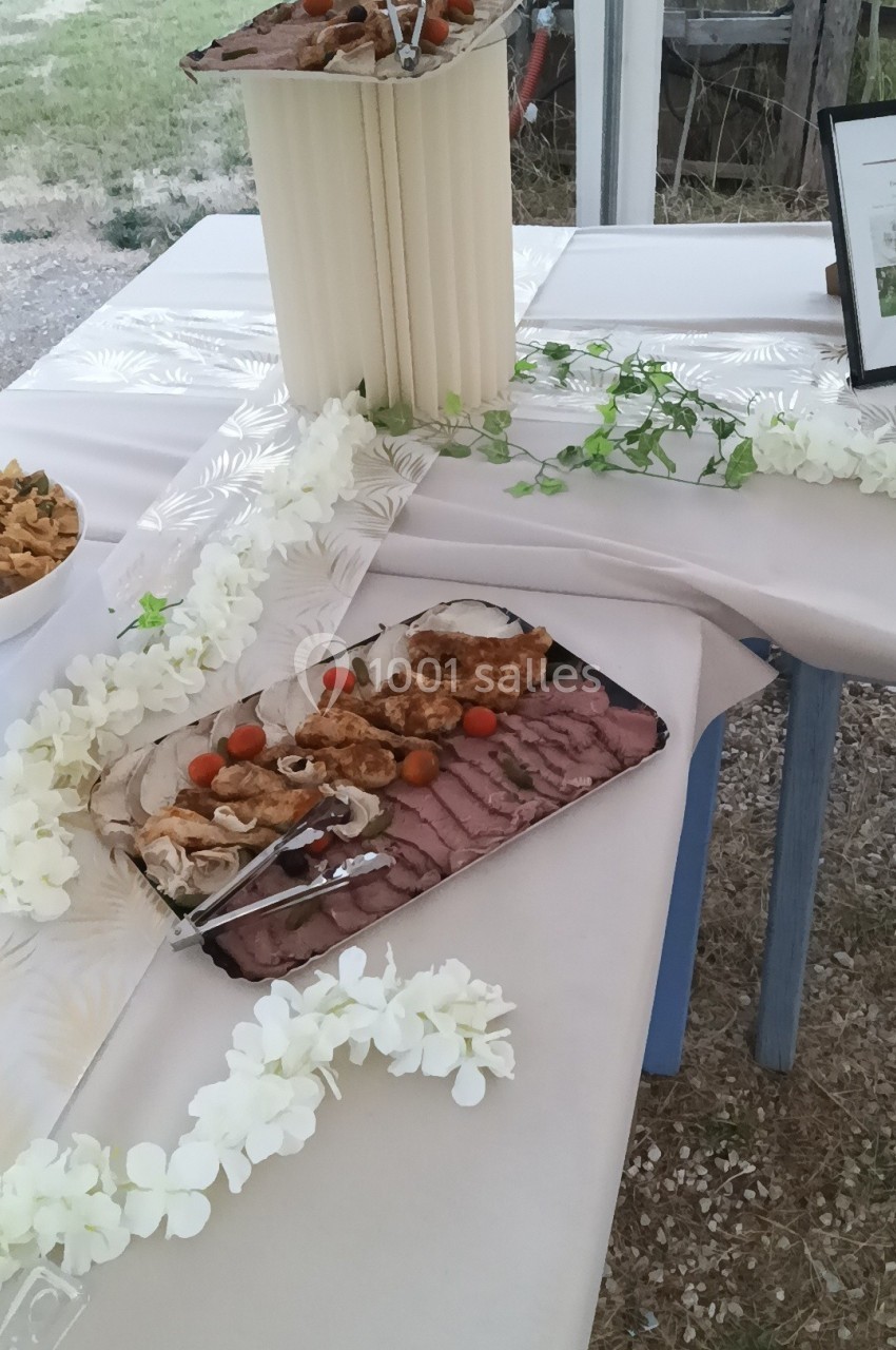 Plateau de viandes grillées et tranchées, accompagné de tomates cerises, disposé sur une table décorée de fleurs blanches.